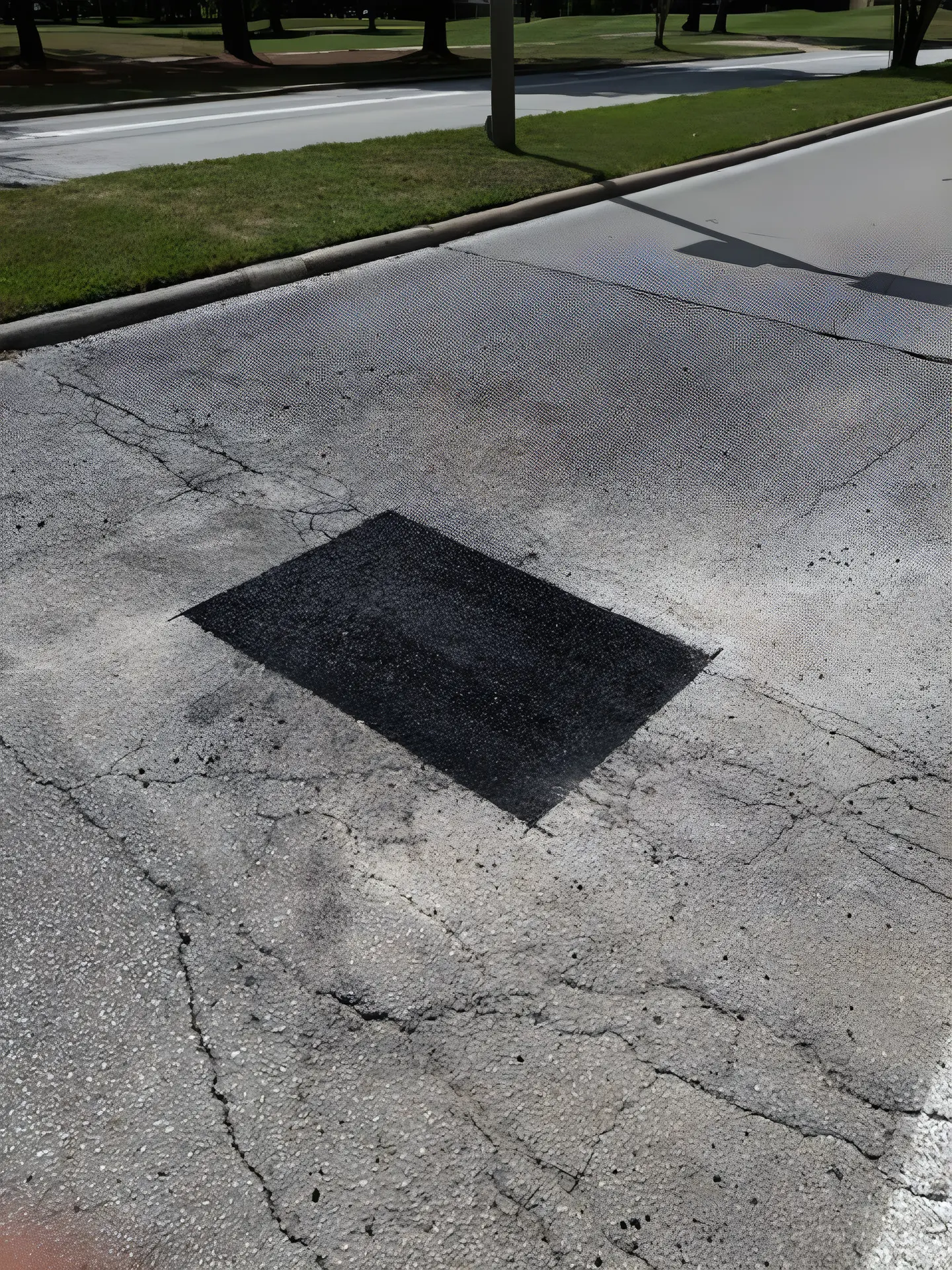Cracked, sun-faded asphalt with a fresh black patch cut into it