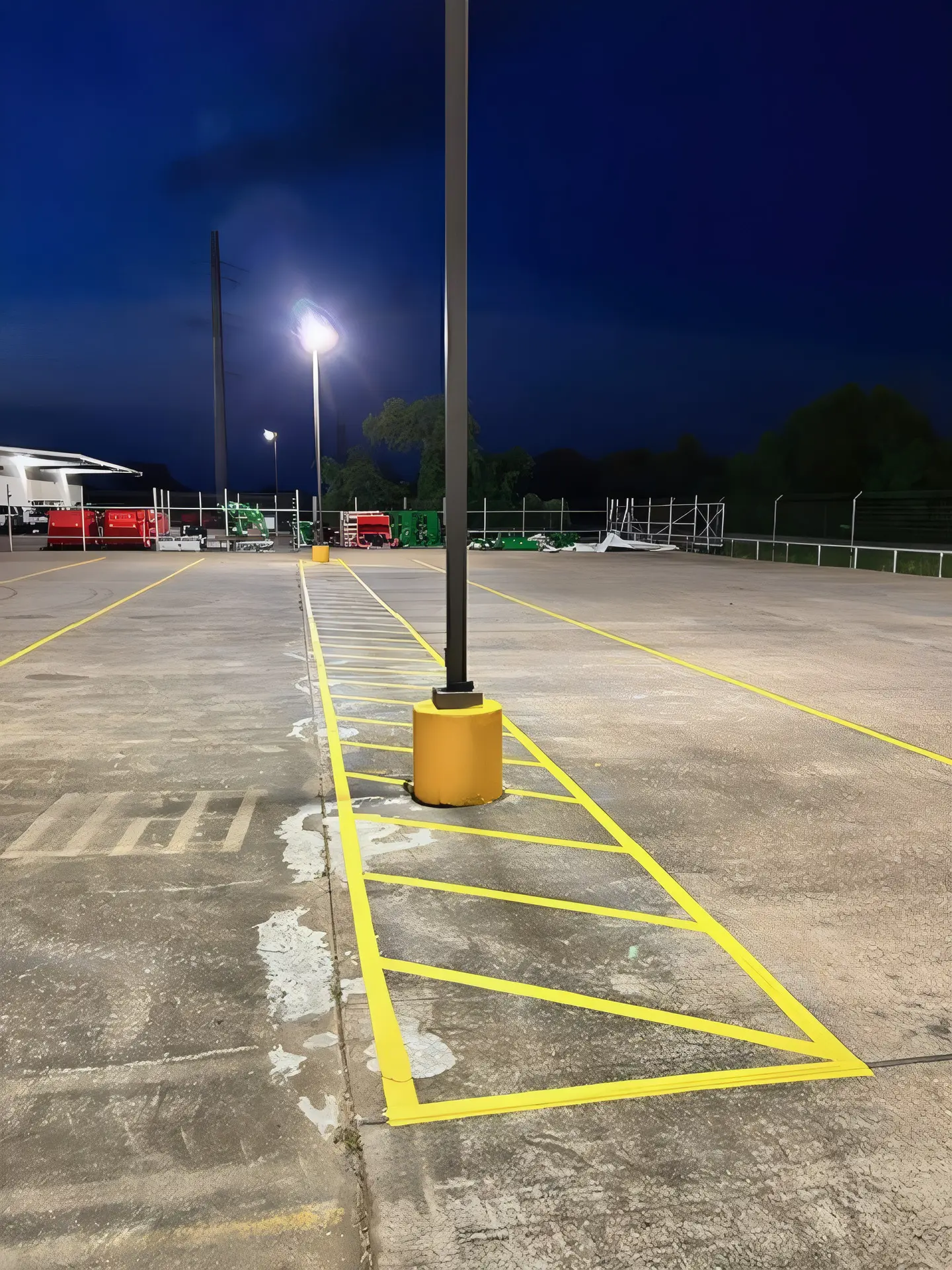 Yellow protective sleeve set over a light pole base inside freshly striped yellow hatching