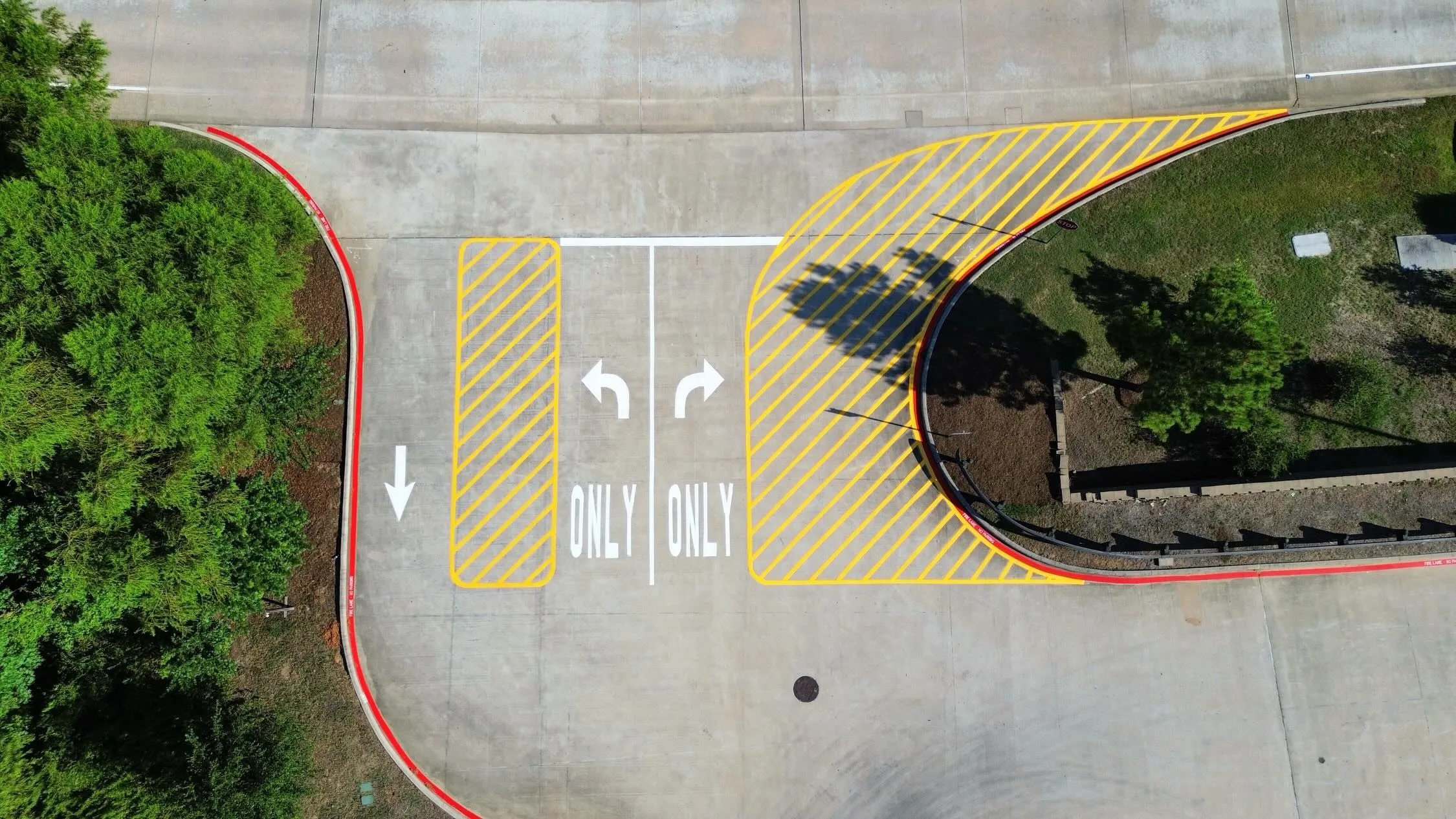 Top-down aerial of a curved red fire lane with yellow hatched zones and painted ONLY turn arrows