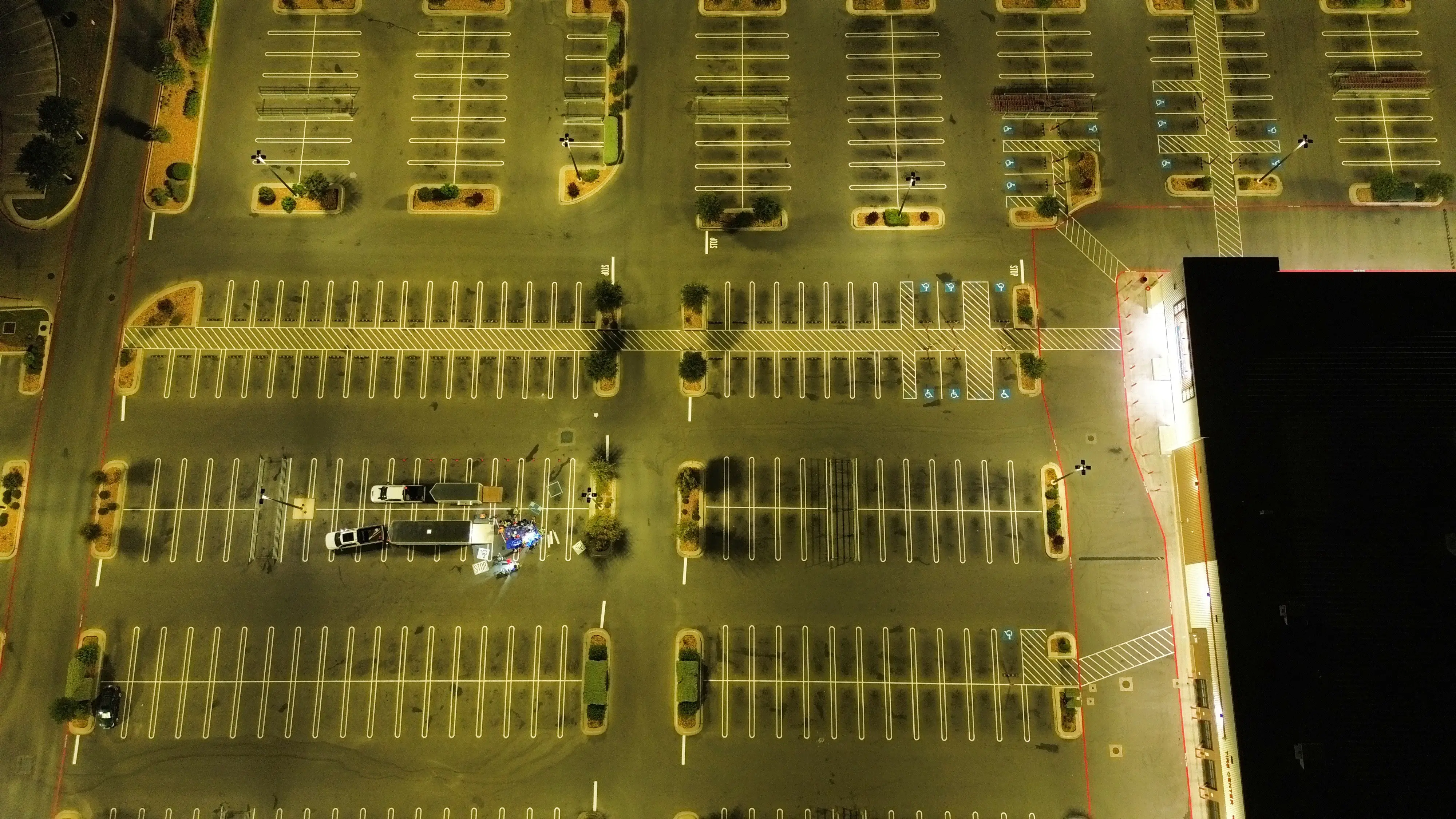 Top-down drone view of a big-box lot at night, every stall freshly striped under the lot lights