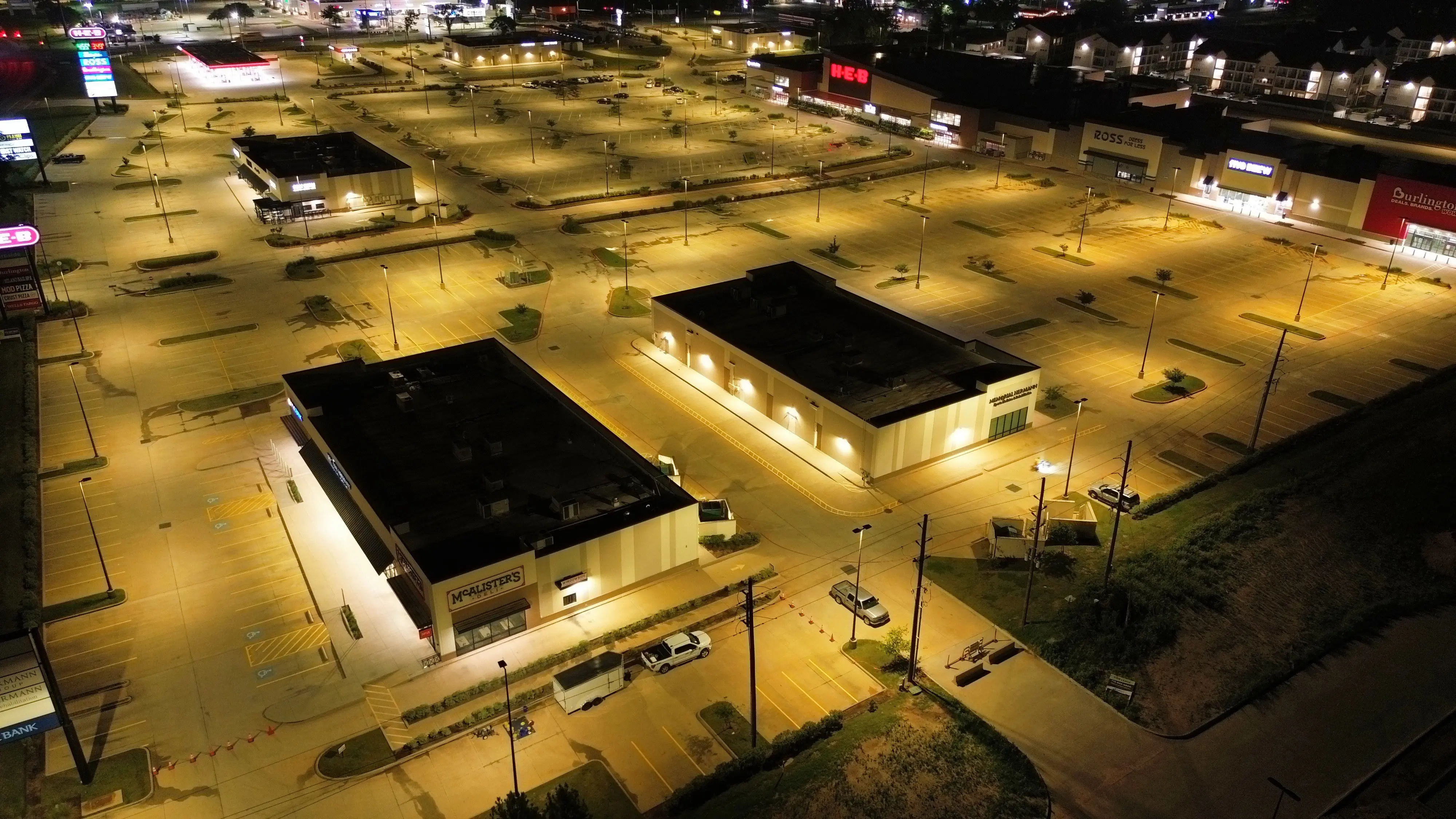 Night aerial of a lit retail center parking lot with fresh stall lines