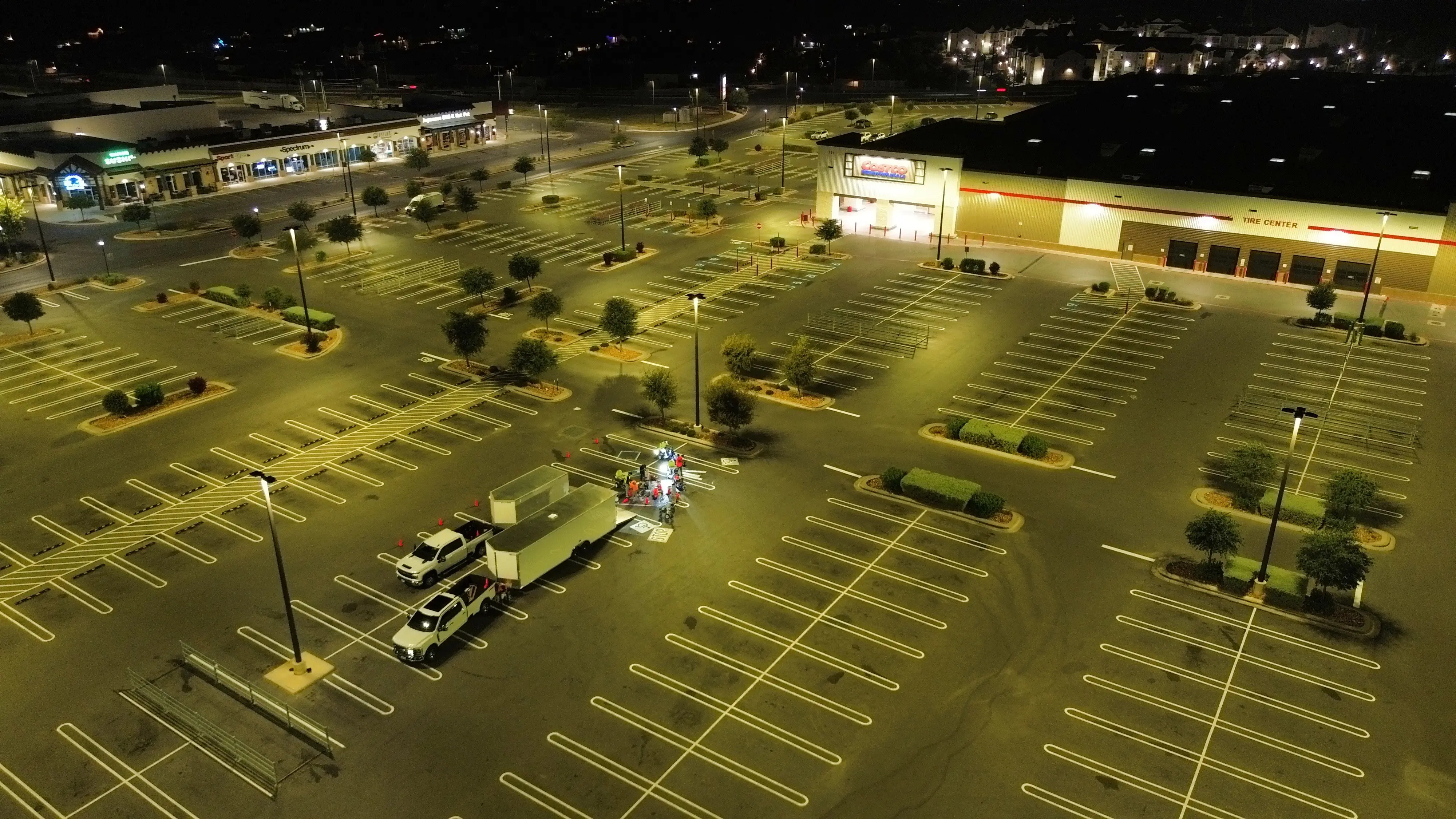 Night aerial of a warehouse club lot with fresh yellow stalls under the lot lights