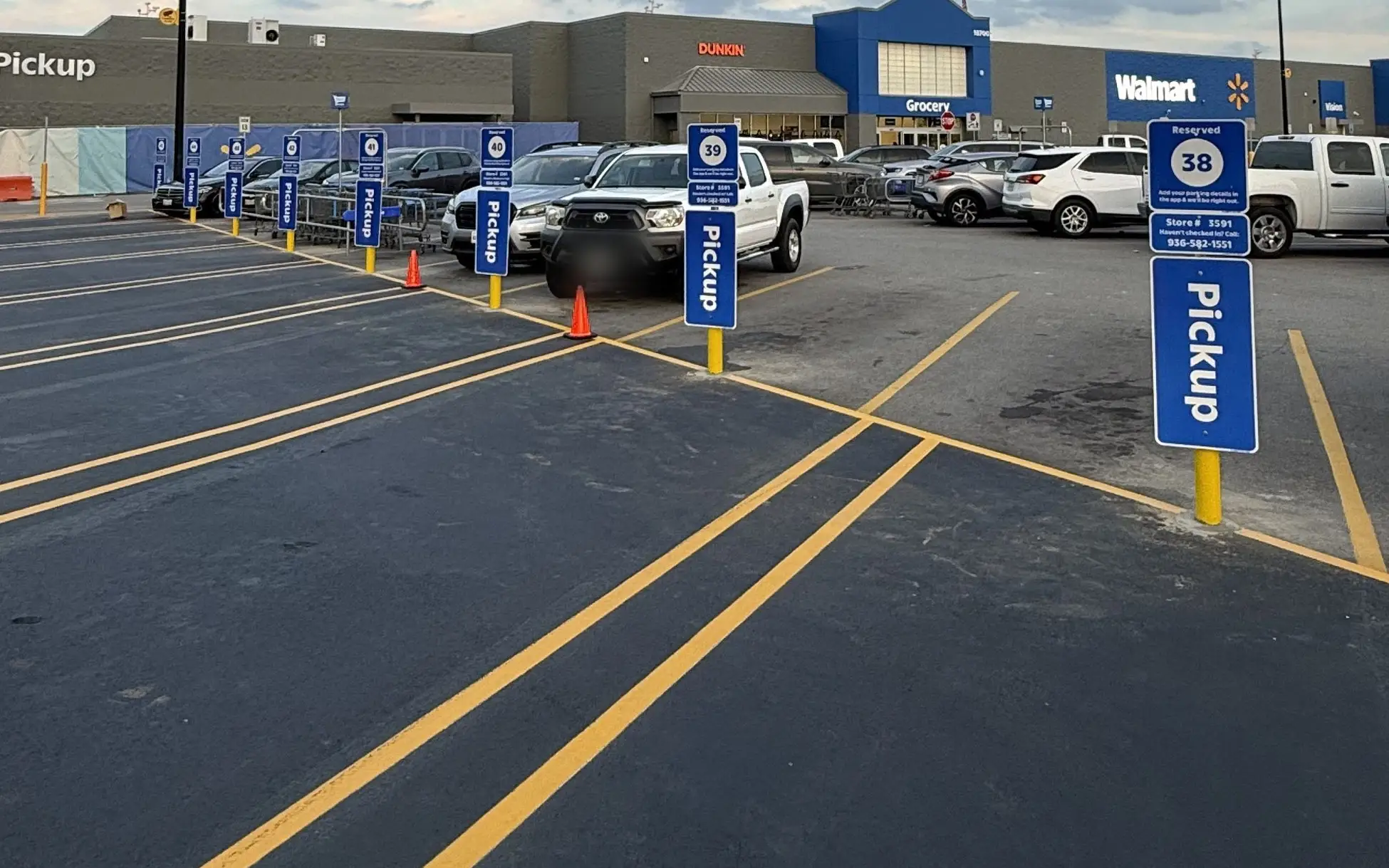 Blue bollards topped with pickup signs along a freshly striped curbside pickup lane