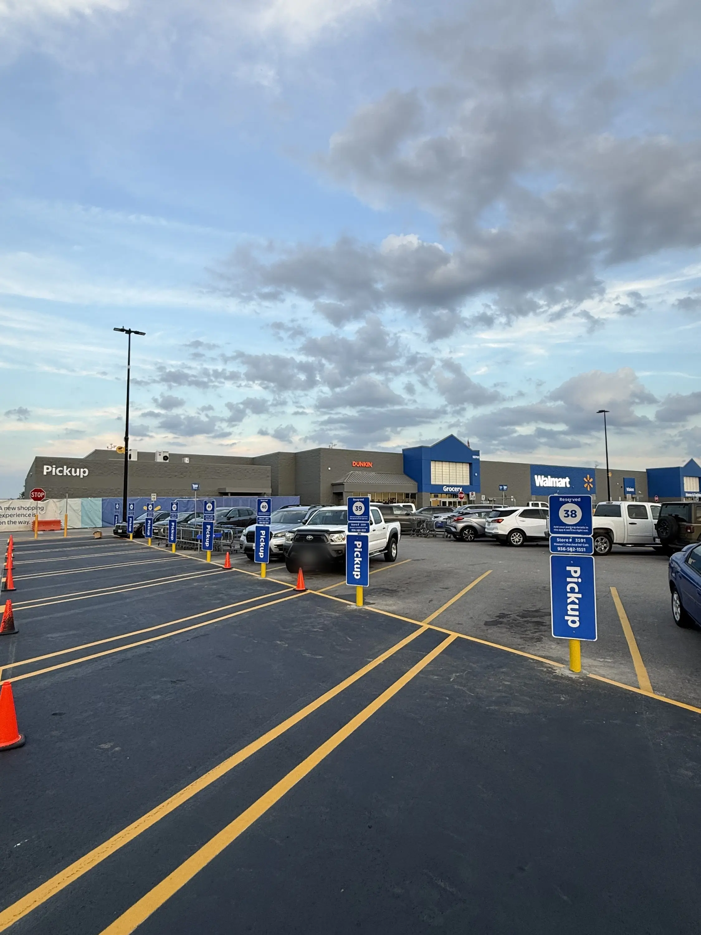 Blue bollards topped with pickup signs along a freshly striped curbside pickup lane
