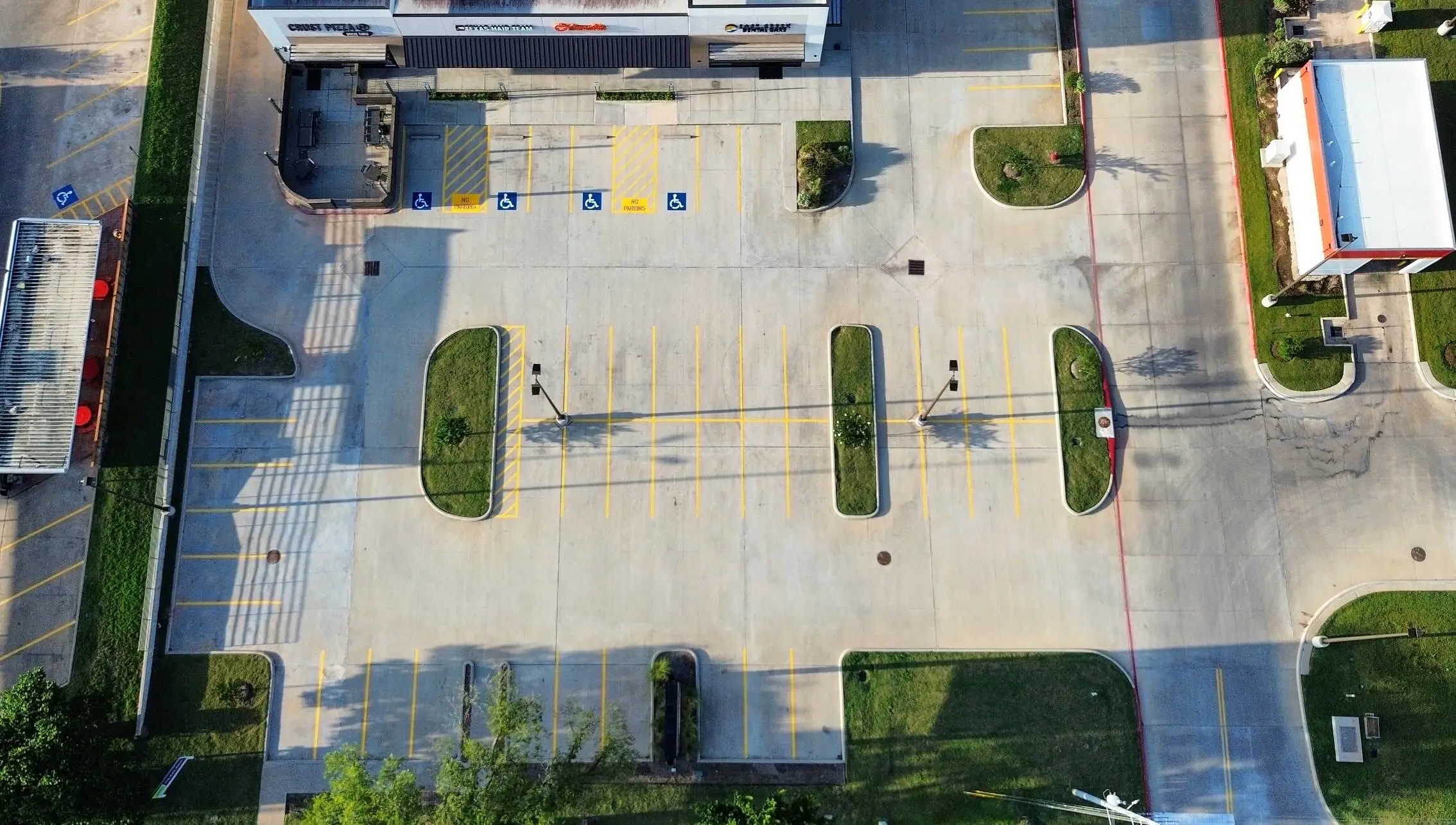 Aerial view of a retail strip center lot with fresh yellow stalls, hatched no-parking zones, accessible symbols, and a red fire lane