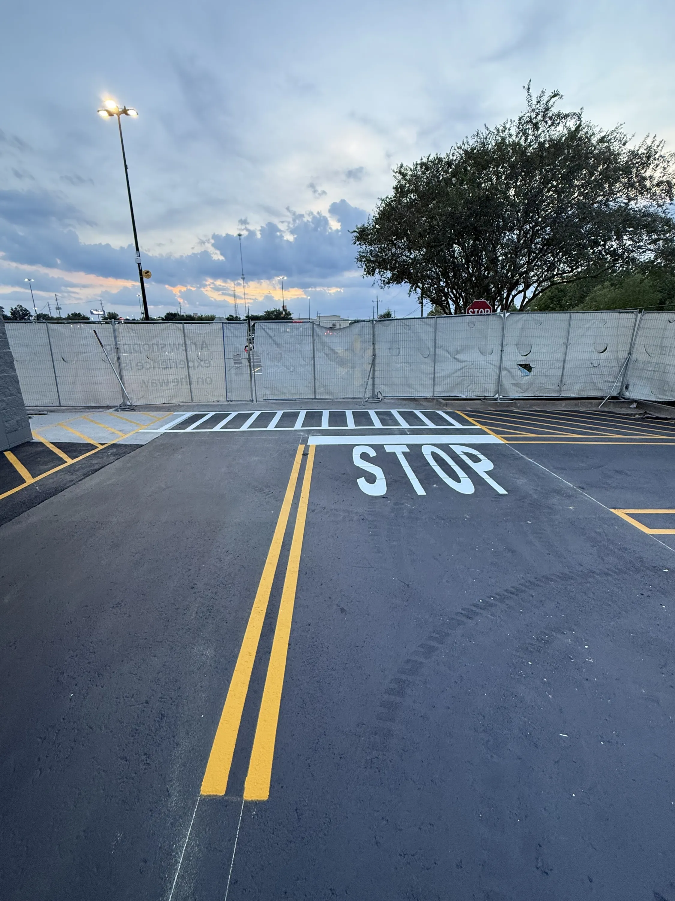 Jet-black sealed asphalt with a fresh yellow double line and STOP stencil, finished by Coastal Roadworks