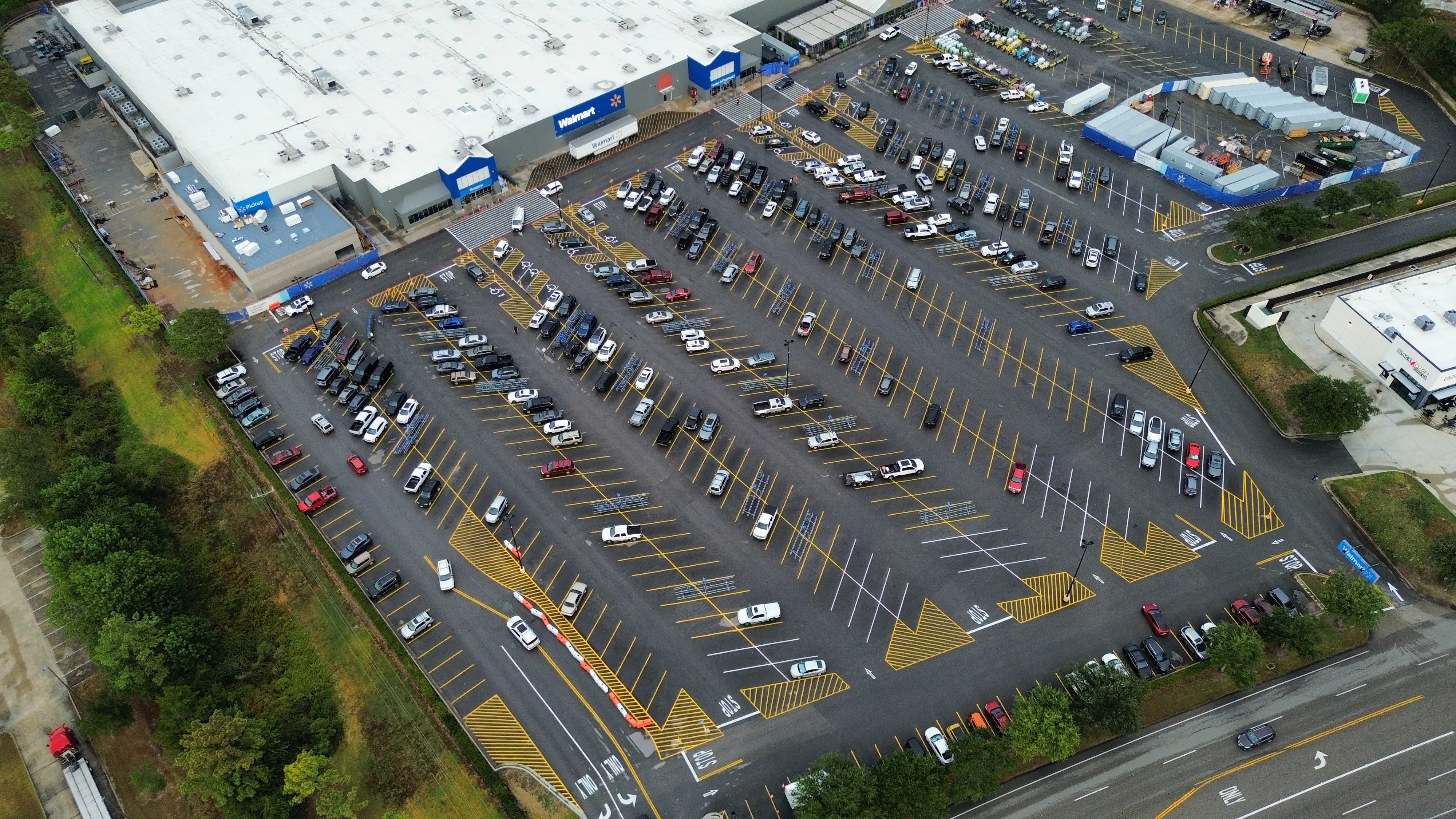 Aerial of a supercenter parking lot in daylight, fresh yellow stalls end to end with the store at the top of the frame