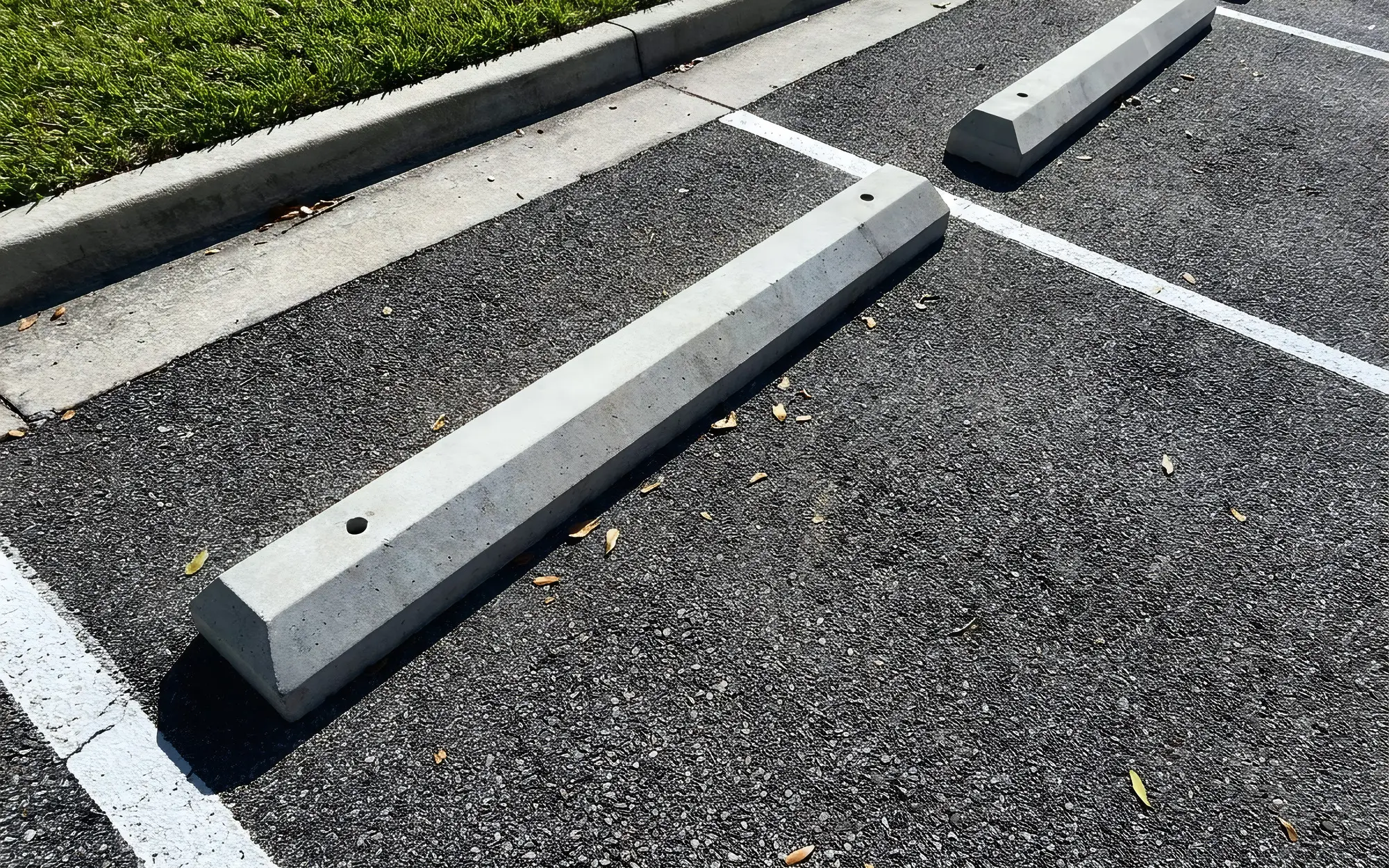 Precast concrete wheel stops pinned at the head of freshly striped parking stalls beside a grass curb
