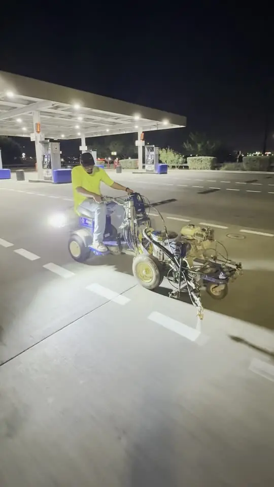 Rider on a line-striping machine laying crisp white dashed lines across a lot at night