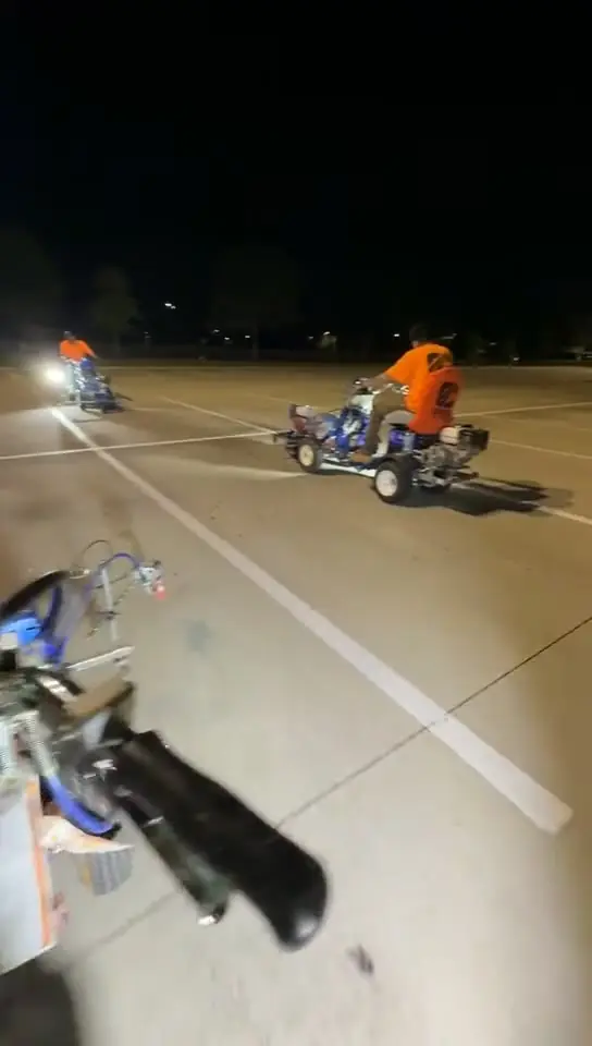Two riding stripers crossing an empty commercial lot at night