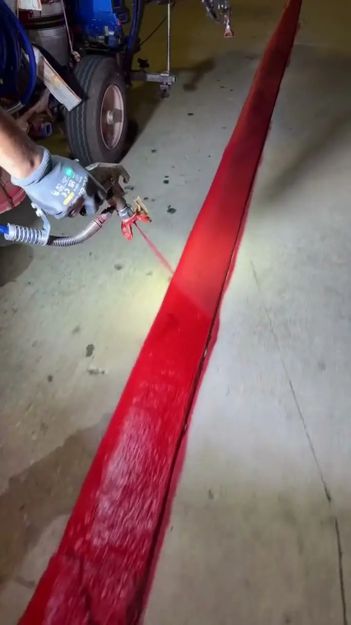 Close view of fresh fire-lane red being sprayed along a curb at night