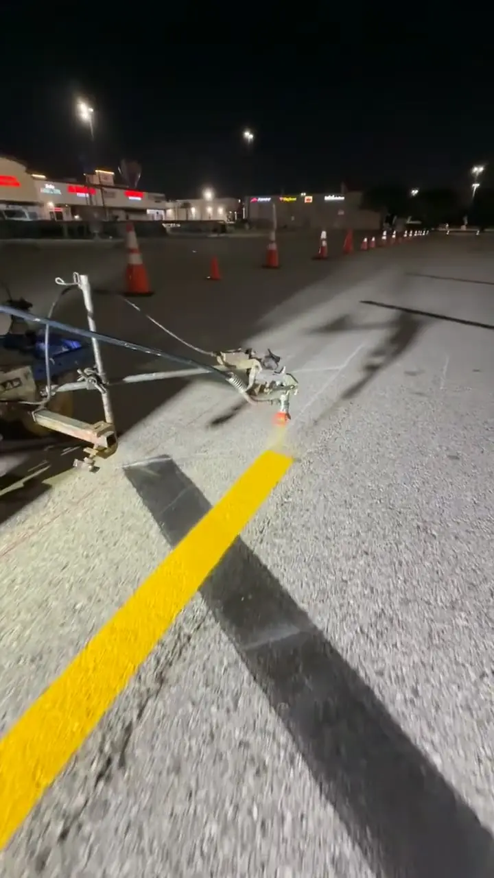 Riding striper laying a fresh yellow line along a landscape bed at night